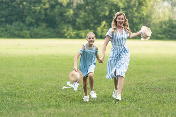 Beautiful mom and daughter holding hands and running on green lawn — Stock Photo