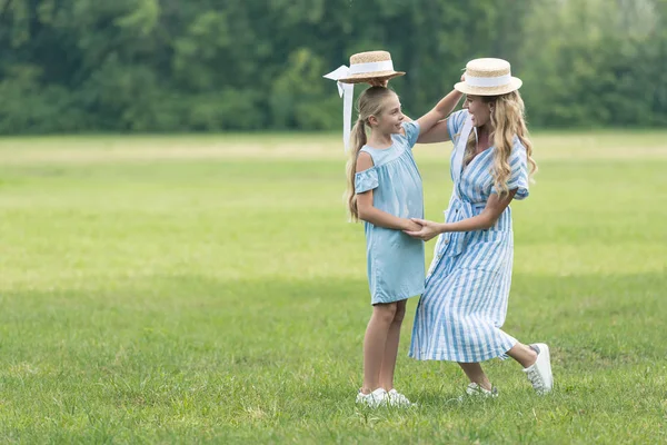 Stylish mother and daughter holding straw hats over heads of each other — Stock Photo