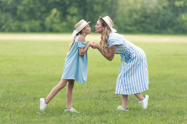 Attraktive Mutter und entzückende Tochter halten Händchen und küssen sich auf grünem Rasen — Stockfoto