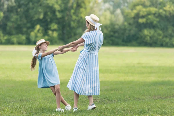Mother and daughter holding hands, twisting and having fun on green lawn — Stock Photo