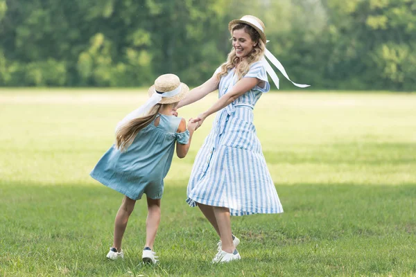Schöne Mutter und Tochter halten Händchen, drehen sich und haben Spaß auf grünem Gras — Stockfoto