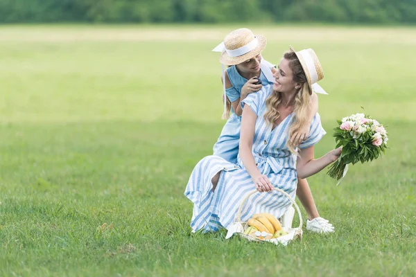 Pai feliz e filha fazendo piquenique com frutas e buquê de flores no gramado verde — Fotografia de Stock
