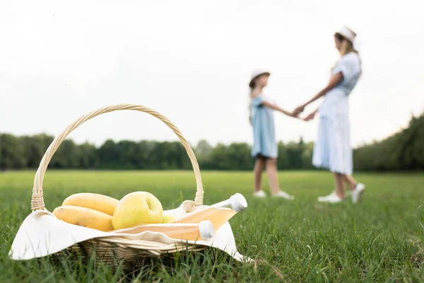 Плетений кошик зі свіжими фруктами і мамою з дочкою на фоні, вибірковий фокус — стокове фото