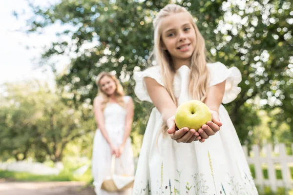 Frühchen-Tochter hält Apfel, junge Mutter mit Weidenkorb im Hintergrund, selektiver Fokus — Stockfoto