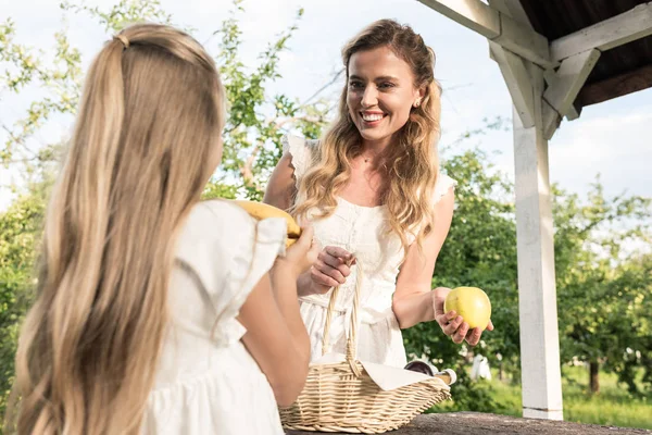 Beautiful mother and adorable daughter with fruits in wicker basket — Stock Photo