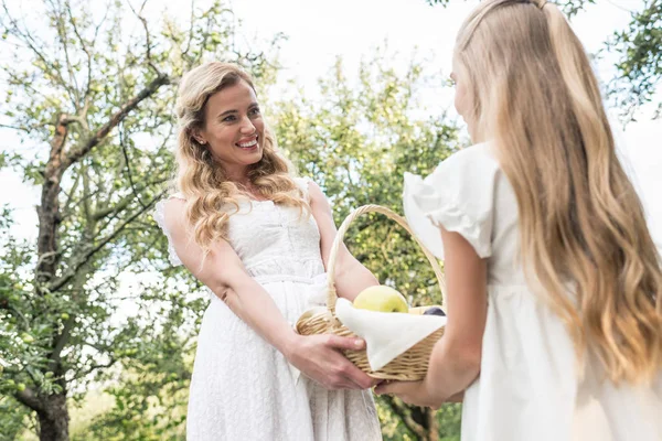 Schöne blonde Mutter und Tochter halten Weidenkorb mit Früchten im Obstgarten — Stockfoto
