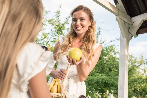 Attractive blonde mother giving apple to her daughter — Stock Photo