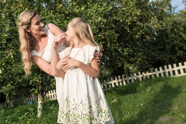 Bionda mamma e figlia in abiti bianchi divertirsi in giardino rurale — Foto stock