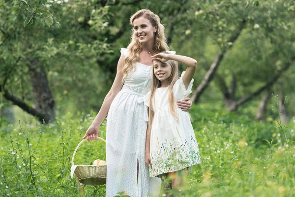Adorable hija y madre sosteniendo cesta de mimbre en huerto - foto de stock