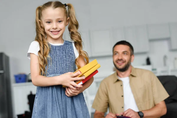 Вибірковий фокус маленької дитини з книгами та батьком позаду вдома, назад до концепції школи — стокове фото