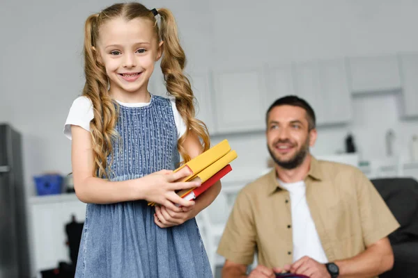 Selective focus of little kid with books and father behind at home, back to school concept — Stock Photo