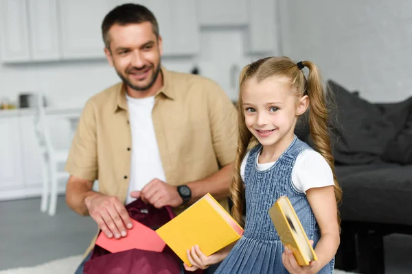 Enfoque selectivo de padre sonriente ayudando a la pequeña hija a empacar la mochila para el primer día en la escuela, volver al concepto de la escuela - foto de stock