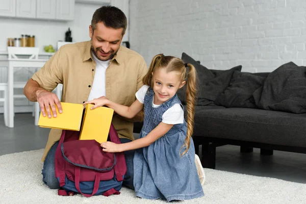 Padre sorridente che aiuta la piccola figlia a imballare lo zaino per il primo giorno a scuola, torna al concetto di scuola — Foto stock