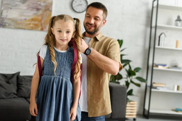 Portrait of father helping daughter to wear backpack at home, back to school concept — Stock Photo