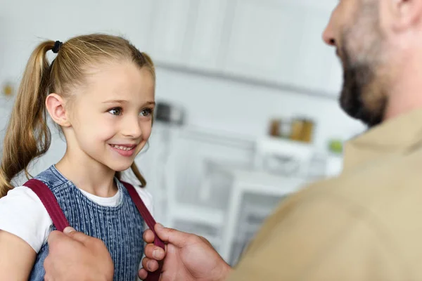 Visión parcial del padre ayudando a su hija a llevar mochila en casa, de vuelta al concepto de la escuela - foto de stock