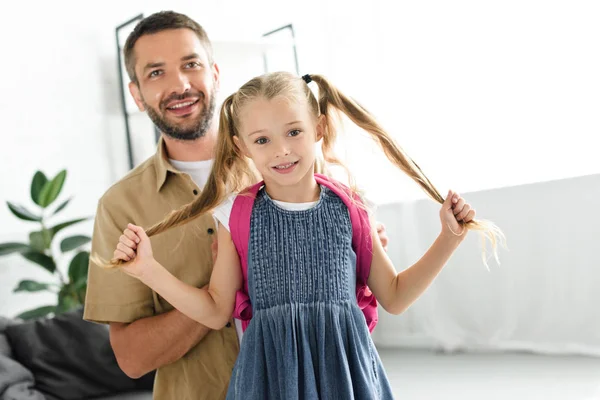 Retrato de padre sonriente e hija pequeña con mochila en casa, concepto de vuelta a la escuela - foto de stock