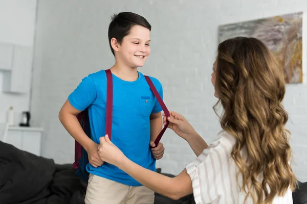 Partial view of mother and smiling boy with backpack at home, back to school concept — Stock Photo