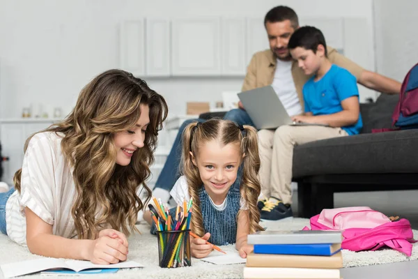 Focalizzazione selettiva della madre che aiuta la figlia con i compiti mentre padre e figlio usano il computer portatile sul divano insieme a casa — Foto stock