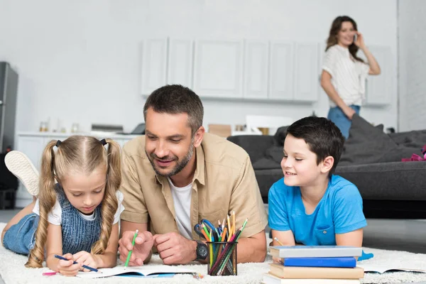 Foco seletivo do pai ajudando as crianças com lição de casa, enquanto a mulher falando no smartphone em casa — Fotografia de Stock