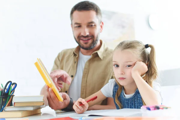 Отец и скучающая дочь делают домашнее задание вместе дома — стоковое фото