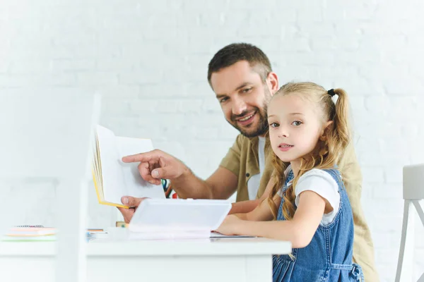 Vue latérale du père et de la petite fille souriants faisant leurs devoirs ensemble à la maison — Photo de stock