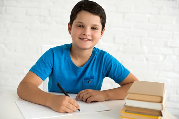 Retrato de menino sorrindo fazendo lição de casa sozinho na mesa em casa — Fotografia de Stock