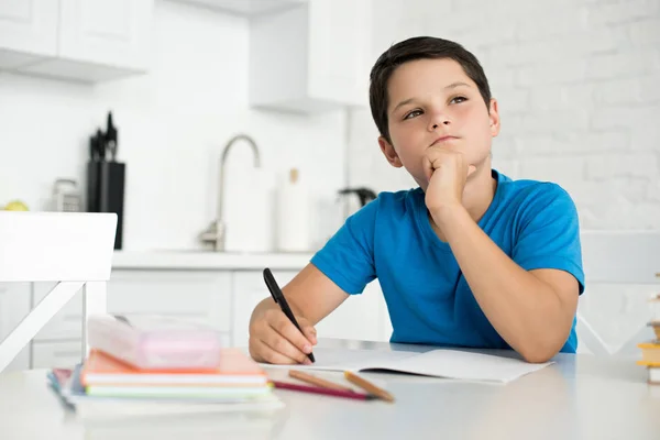 Portrait d'un garçon réfléchi faisant ses devoirs seul à table à la maison — Photo de stock