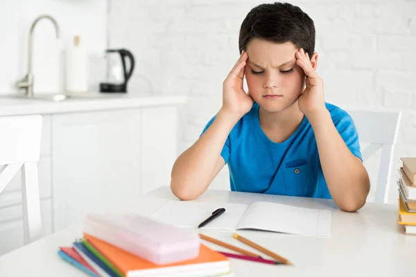 Retrato del niño enfocado sentado en la mesa con copybook, bolígrafo y cuadernos en casa - foto de stock