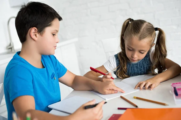 Frère et sœur faisant leurs devoirs ensemble à table à la maison — Photo de stock