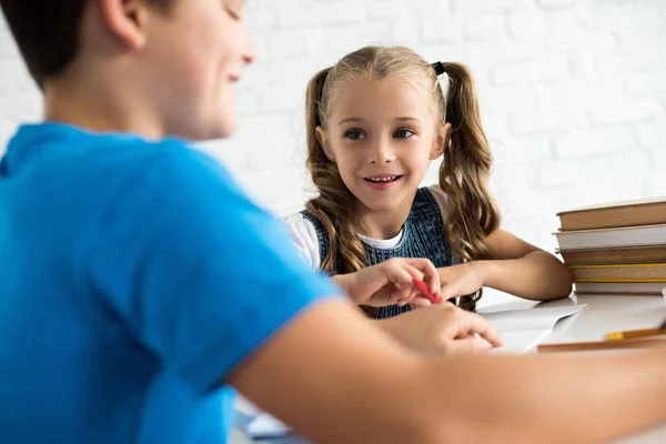 Частичный вид брата и улыбающаяся сестра делают домашнее задание вместе за столом дома — стоковое фото