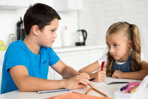 Retrato del hermano y la hermana haciendo los deberes juntos en la mesa en casa - foto de stock