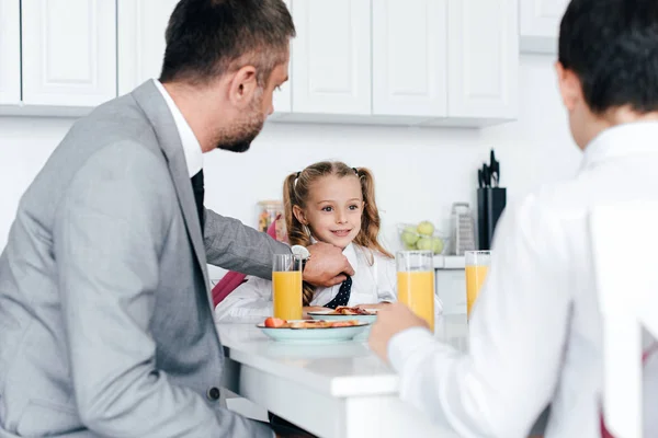 Partial view of father and kids in school uniform having breakfast at home — Stock Photo