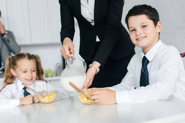 Vista parcial de los niños en uniforme escolar y los padres durante el desayuno en casa, de vuelta al concepto escolar - foto de stock