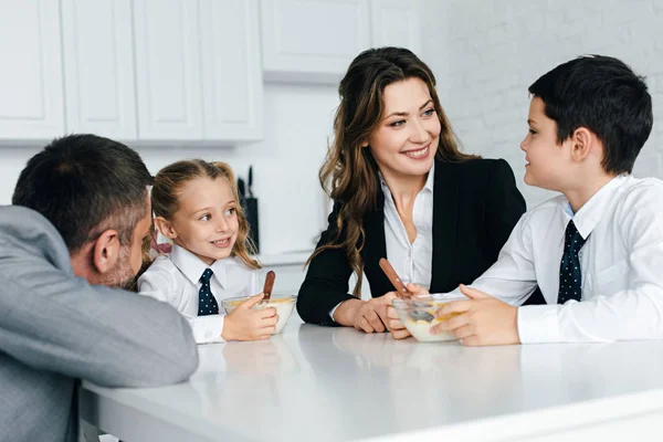 Família em ternos e uniforme escolar tomando café da manhã na cozinha juntos — Fotografia de Stock