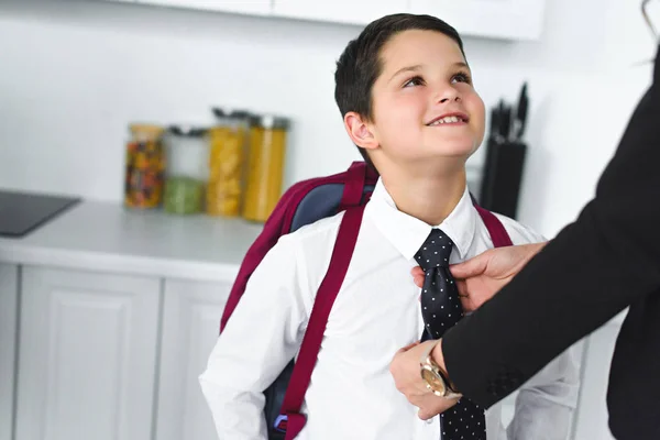 Partial view of mother in suit tying sons tie in kitchen at home, back to school concept — Stock Photo