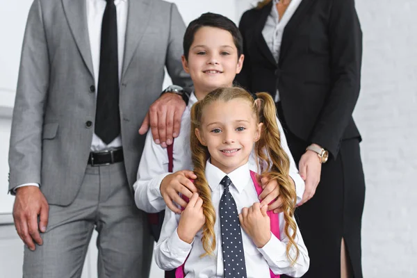 Частичный вид улыбающихся детей в школьной форме и родителей в костюмах дома — стоковое фото