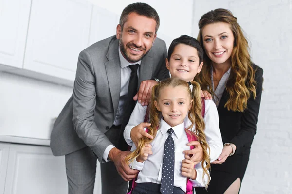 Portrait of smiling kids in school uniform with backpacks and parents in suits at home — Stock Photo