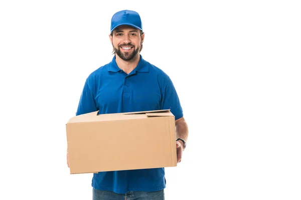 Guapo feliz joven repartidor sosteniendo caja de cartón y sonriendo a la cámara aislada en blanco - foto de stock