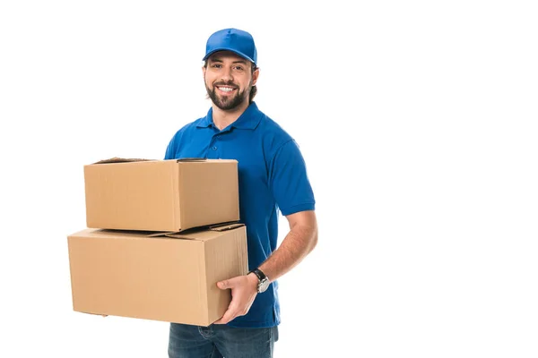 Guapo feliz joven repartidor sosteniendo cajas de cartón y sonriendo a la cámara aislado en blanco - foto de stock