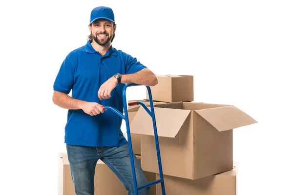 Handsome happy delivery man standing near cardboard boxes and smiling at camera isolated on white — Stock Photo