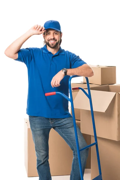 Homem de entrega bonito de pé perto de caixas de papelão e sorrindo para a câmera isolada em branco — Fotografia de Stock