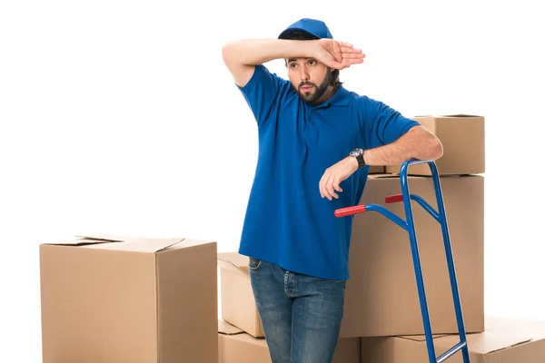 Tired delivery man standing between cardboard boxes and looking away isolated on white — Stock Photo