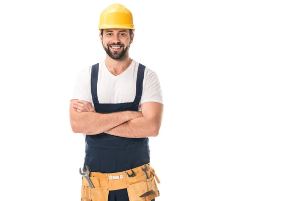 Belo trabalhador feliz em chapéu duro e cinto de ferramentas de pé com braços cruzados e sorrindo para a câmera isolada no branco — Fotografia de Stock