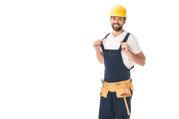 Guapo trabajador feliz en cinturón de herramientas y sombrero duro sonriendo a la cámara aislada en blanco - foto de stock