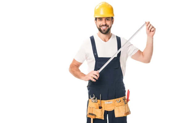 Guapo trabajador feliz sosteniendo cinta métrica y sonriendo a la cámara aislado en blanco - foto de stock