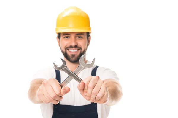 Handsome happy workman in hard hat holding wrenches and smiling at camera isolated on white — Stock Photo