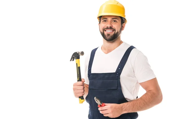 Apuesto obrero sonriente sosteniendo alicates y martillo aislado en blanco - foto de stock