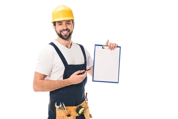 Trabajador de la construcción feliz en sombrero duro y cinturón de herramientas sosteniendo portapapeles en blanco y sonriendo a la cámara aislada en blanco - foto de stock