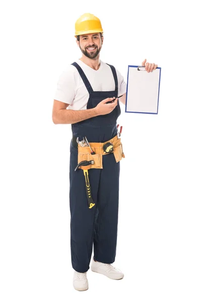 Trabajador de la construcción guapo en cinturón de herramientas sosteniendo portapapeles en blanco y sonriendo a la cámara aislada en blanco - foto de stock