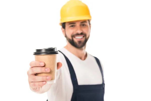 Vista de cerca de trabajador feliz en el sombrero duro sosteniendo taza de papel con café para ir y sonriendo a la cámara aislada en blanco — Stock Photo